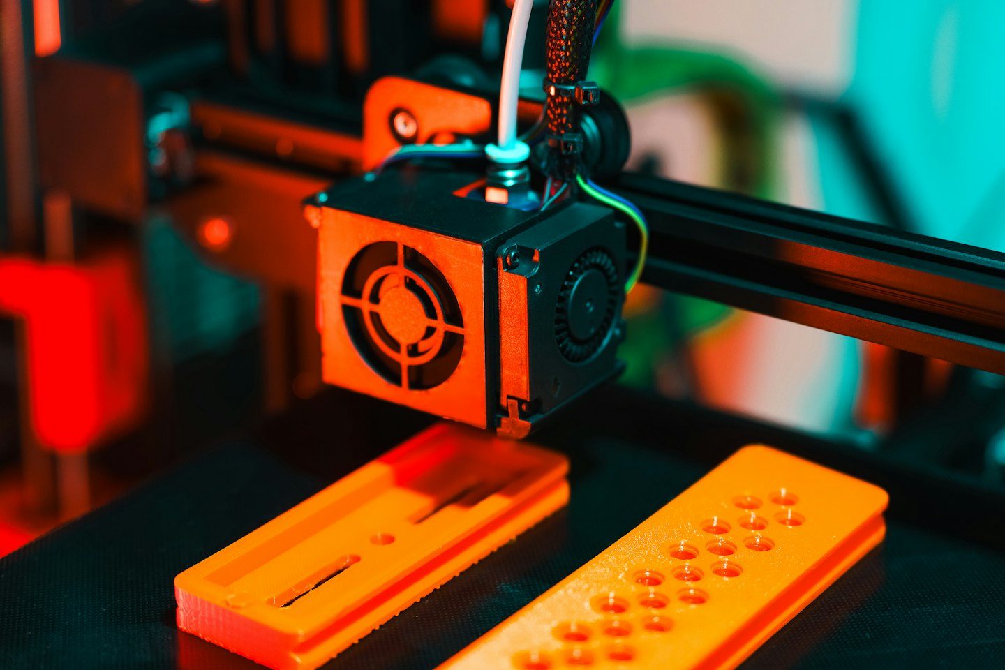 3D printer extruding orange filament on a build plate.